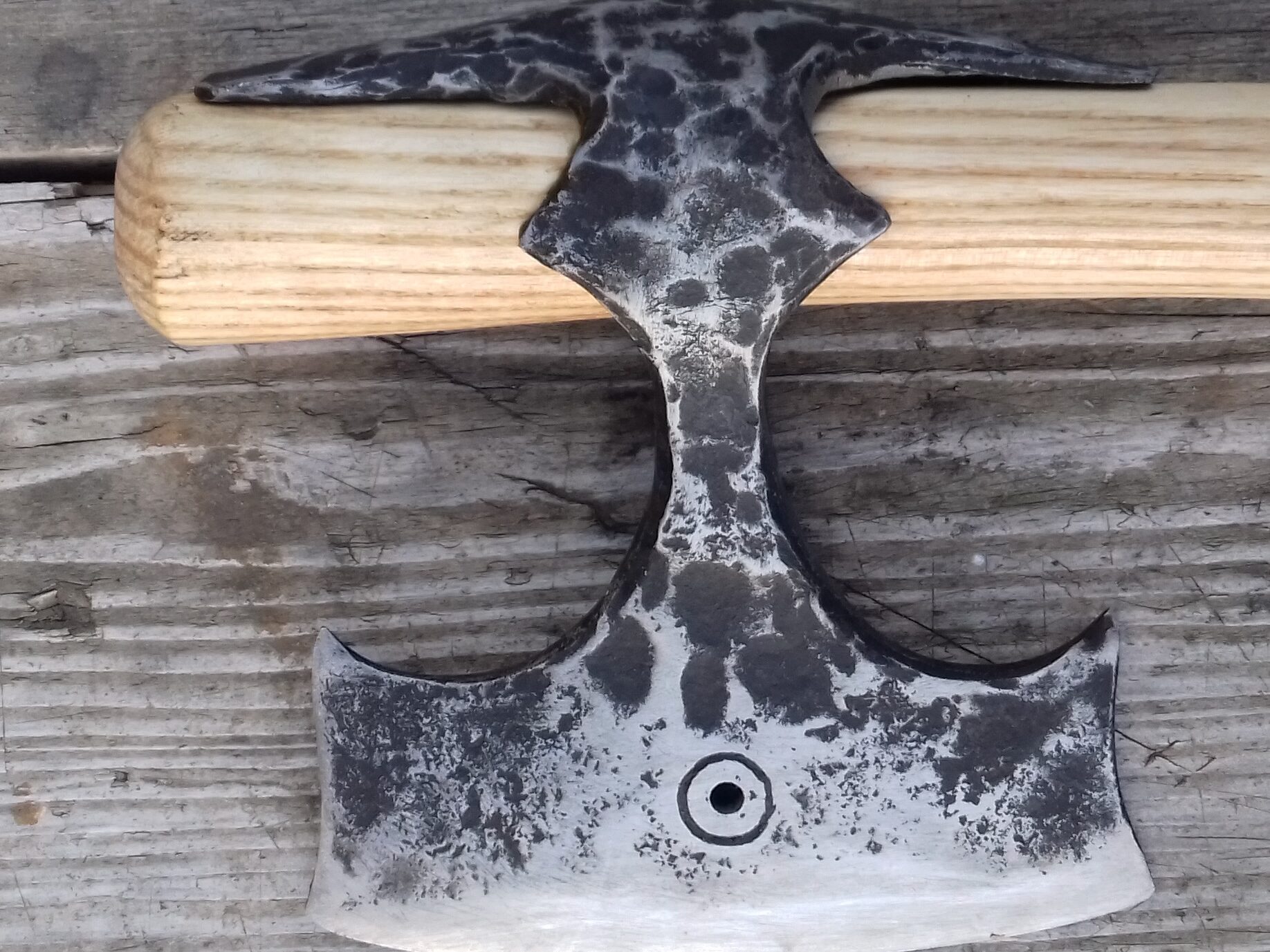 Hand-forged axe with light wood handle on weathered wood background